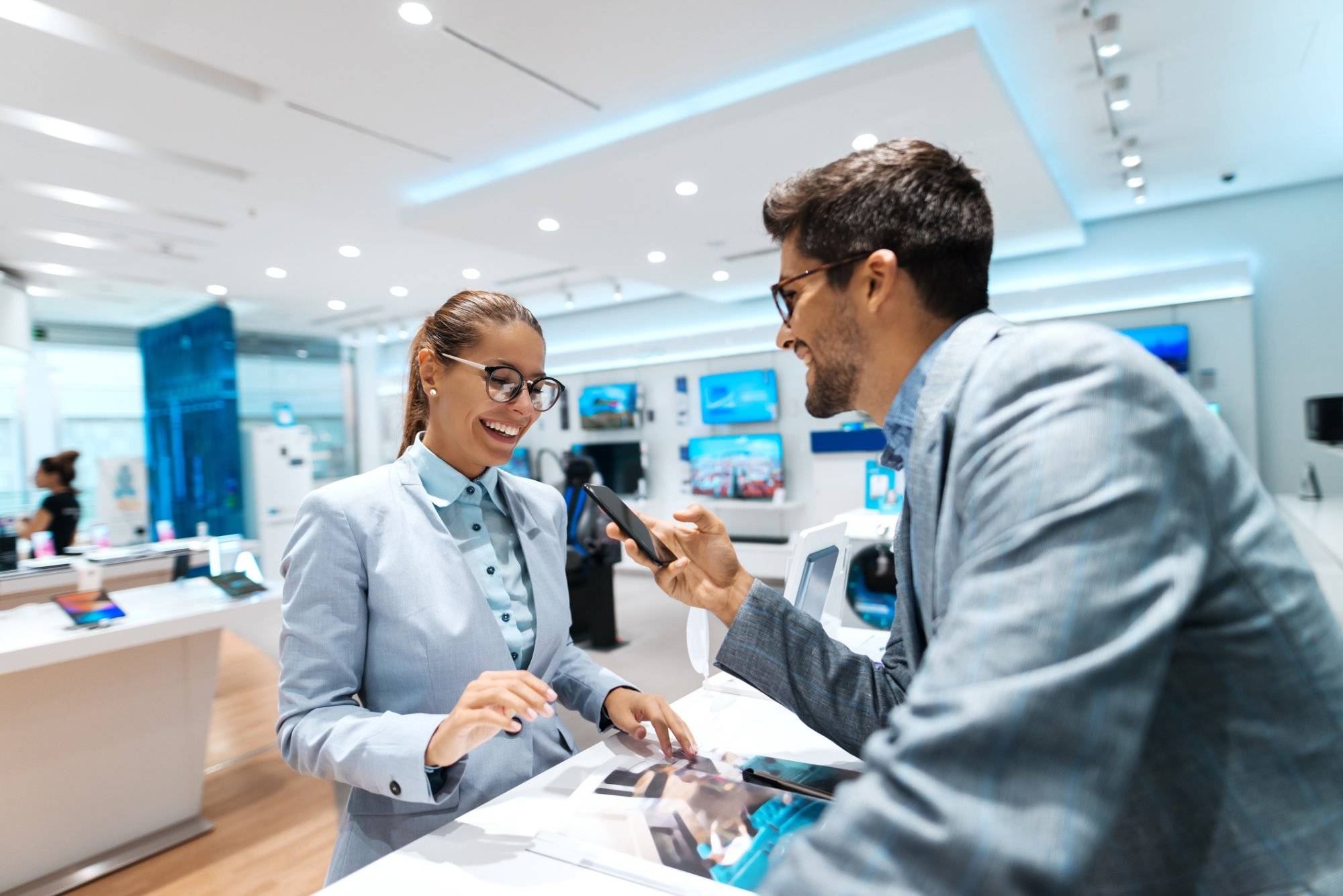 Young multicultural couple looking for new smart phone to buy. Woman looking at catalog while man holding smart phone.