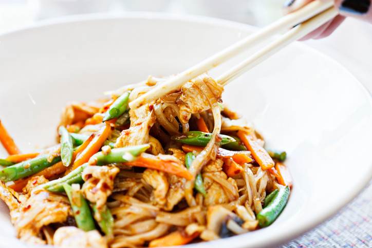 Woman's hand uses chopsticks to serve Thai chicken noodle dish